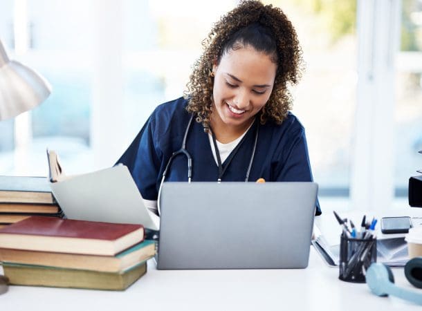 Smiling nurse studying with laptop and books.